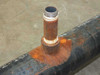 Close-up of threaded NPT pipe nipple welded to main pipe body, showing rust and pipe threads with PTFE tape residue