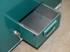 Locking storage drawer at base of rivet station cabinet — dark green painted steel drawer with key lock cylinder, partially opened showing empty interior