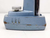 Close-up of microscope stand base showing gray fine-adjustment knob, cast metal housing, and paint wear with rust spots