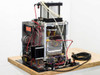 Rear view of press assembly showing pneumatic cylinder, spring platen, control wiring, and solenoid valves on base