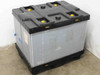 JSI JSI-0047 collapsible plastic bulk container shown fully assembled and expanded on warehouse floor, front view with grey walls and black lid with yellow latches