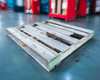 Single 48x48 wooden pallet on warehouse floor at low angle showing deck and green-painted stringer ends