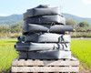 Multiple Toro Blueline 4-inch oval irrigation hose rolls stacked on a pallet with green farmland in the background