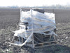 Three-quarter view of used polyethylene irrigation tubing pallet lot wrapped in clear plastic, sitting on a wooden pallet in a plowed agricultural field