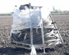 Side view of pallet lot of used poly drip irrigation hose coils and sections bundled together on a wooden pallet in a farm field