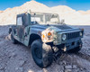 AM General M1152 HMMWV front three-quarter view showing camouflage paint, exterior wear and body damage visible on hood and fender