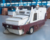 PowerBoss TSS/80-HD propane riding sweeper scrubber — front three-quarter view showing side brush, front bumper, and white and maroon body in warehouse