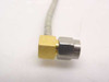 Close-up of opposite right-angle SMA male connector end showing gold brass hex body and stainless steel mating pin on braided semi-rigid coax