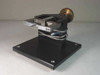 Custom calibration fixture front-left view showing XY adjustment stage, spring-loaded probe holder, brass knurled actuator knob, and black anodized base plate with rubber feet