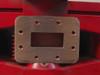 CPI VKC-7936 waveguide output flange close-up — machined rectangular WR-137 waveguide flange with eight mounting holes on red chassis background