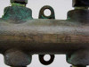 Close-up of brass manifold body showing surface patina, verdigris oxidation, and stamped markings on the barrel