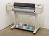 HP DesignJet 2500CP C4704A wide format color plotter on rolling stand, front view with ink cartridge boxes on lower shelf