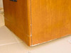 Close-up of desk pedestal lower corner showing finish marring and laminate separation at the base edge