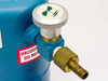 Close-up of vacuum valve assembly on blue dewar body — knurled aluminum needle valve, brass barbed fitting, and red 'VACUUM DO NOT...' warning label