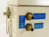 ISA Riber CX 700 water connection panel close-up showing brass barb fittings labeled Water Output (top) and Water Input (bottom) with blue labels and security chain