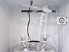Close-up of top of stainless steel chemical canister inside FSI ChemFill cabinet showing polypropylene inlet/outlet tubing connections, liquid level sensor, and top-mount fittings