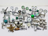 Large mixed lot of approximately 20 gas pressure regulators, valves, and gauges spread out on white surface — chrome, brass, and stainless pieces including dual-gauge regulators and inline valves