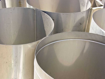 Close-up of large stainless steel round cylindrical duct sections showing corrugated locking seam at base
