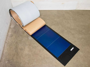Uni-Solar PVL-136 136W flexible solar panel partially unrolled from cardboard core showing full panel length on warehouse floor