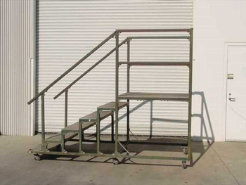 Mobile steel work platform with diamond plate steps and 42-inch safety rails on lockable casters — side angle view showing stair ascent and upper deck frame