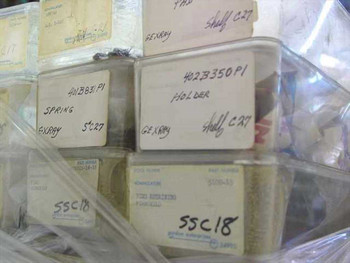 Close-up of individual parts bins showing handwritten labels with part numbers and nomenclature — Gordon Enterprises stock tags visible