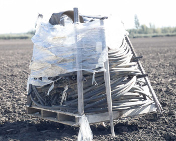 Side view of pallet lot of used poly drip irrigation hose coils and sections bundled together on a wooden pallet in a farm field