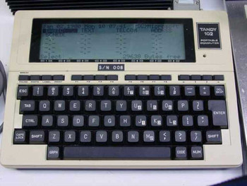 Tandy 102 Portable Computer front view – LCD display showing menu, QWERTY keyboard, S/N 008 label visible below screen