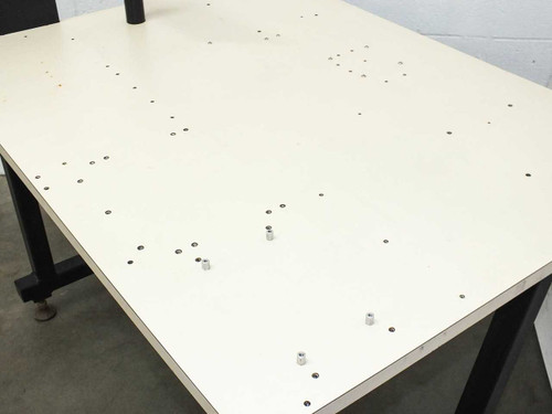 Close-up of white steel table surface showing numerous threaded feed-through holes and two installed hex standoffs