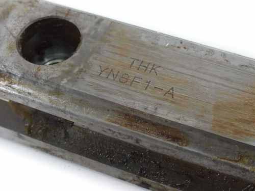 Close-up of THK YN8F1-A model number stamped on carriage block, showing grease and surface wear