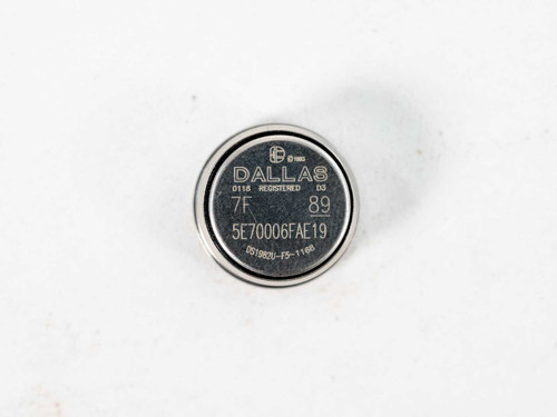 Close-up of single Dallas Semiconductor DS1982U-F5 iButton showing engraved serial number 5E70006FAE19 and date code 89, top face view