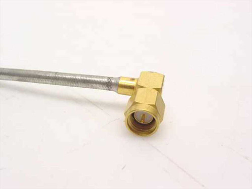 Close-up of SMA male right angle connector on semi-rigid coax cable — gold-plated brass body, 90-degree bend, braided silver outer jacket