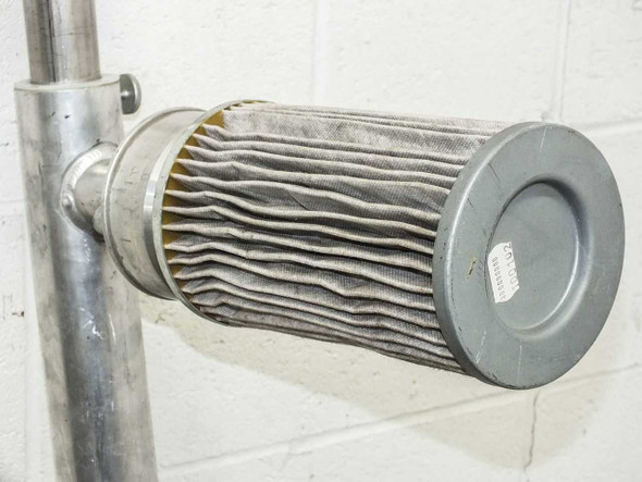 Close-up of cylindrical pleated filter element showing corrugated filter media and end cap with label, mounted on aluminum pole