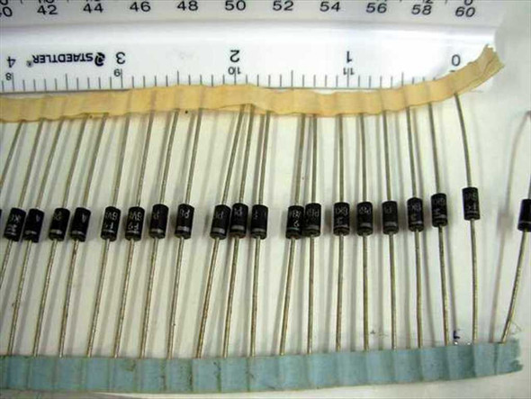Lot of STMicroelectronics P6KE6V8A TVS diodes banded together in a row on tape strip with ruler showing scale