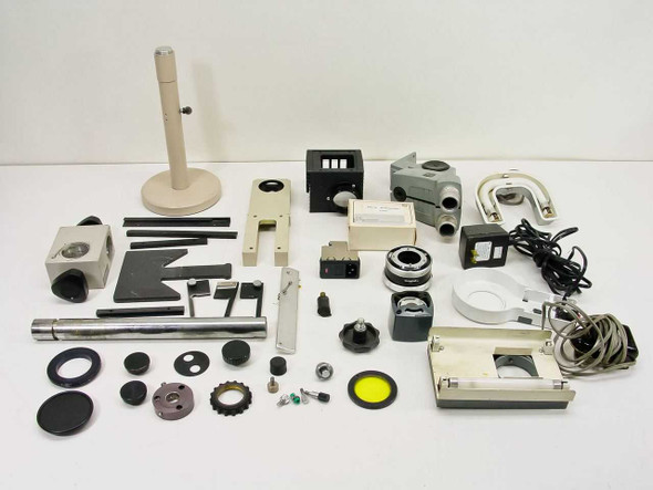 Full overhead view of approximately 36 mixed microscope parts spread on white surface including stand, heads, filter cubes, ring lights, knobs, and adapters