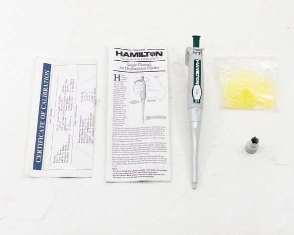 Hamilton 55019-05 25µL SoftGrip pipette with certificate of calibration, manual, calibration tool, and bag of yellow pipette tips laid out on white surface