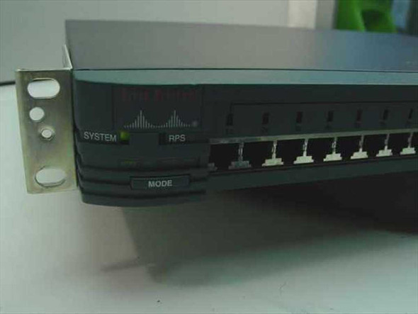 Cisco WS-C2924XL — left-front angle showing rack ear, MODE button, SYSTEM and RPS LED indicators, and uplink ports; cracked front-right corner plastic visible