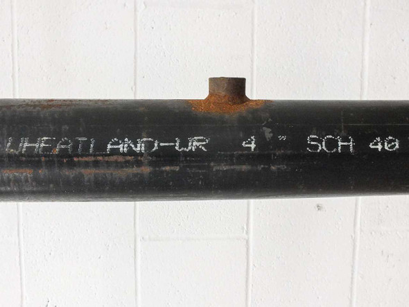Close-up of pipe body markings reading WHEATLAND-UR 4 SCH 40 with visible surface rust and black coating