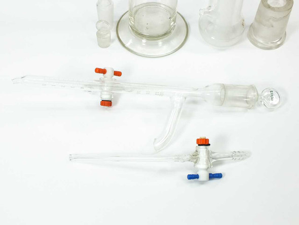Lot of assorted laboratory glassware including tall graduated cylinder, adapter, buret with stopcocks, and small vials — overview