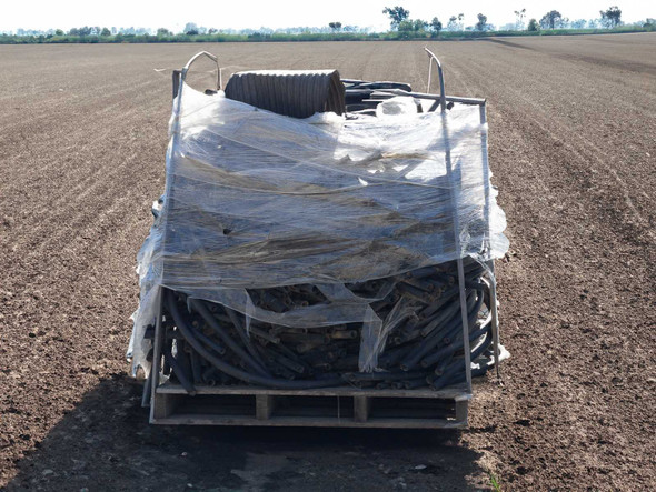 Pallet of used agricultural polyethylene drip irrigation tubing in assorted sizes, wrapped in plastic sheeting, photographed in an open farm field — full front view