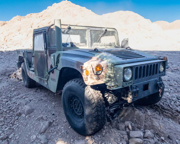 AM General M1152 HMMWV front three-quarter view showing camouflage paint, exterior wear and body damage visible on hood and fender