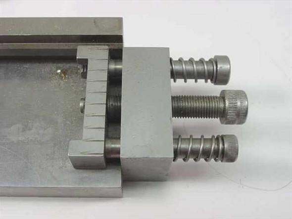Close-up of IC test fixture jig showing adjustable clamping block with two knurled thumb screws and graduated scale