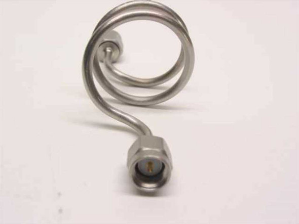 Close-up front view of SMA male connector end on stainless steel coiled semi-rigid coaxial cable showing gold center pin