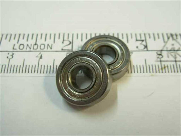 Steel miniature double-shielded ball bearing 1/4 inch bore shown alongside a ruler for scale — front face view of two bearings