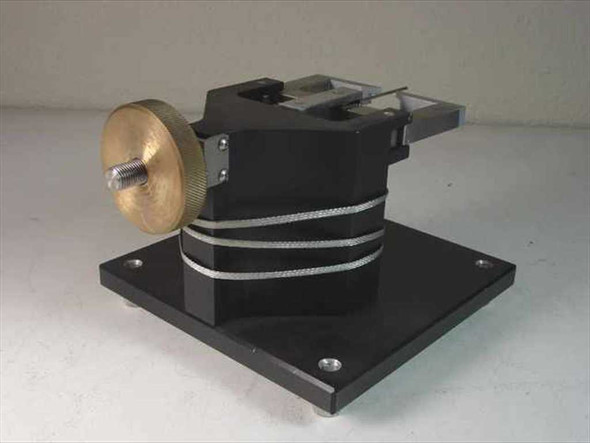 Custom calibration fixture rear-right view showing brass knurled actuator knob, braided wire harness wrapped around black body, and flat base plate