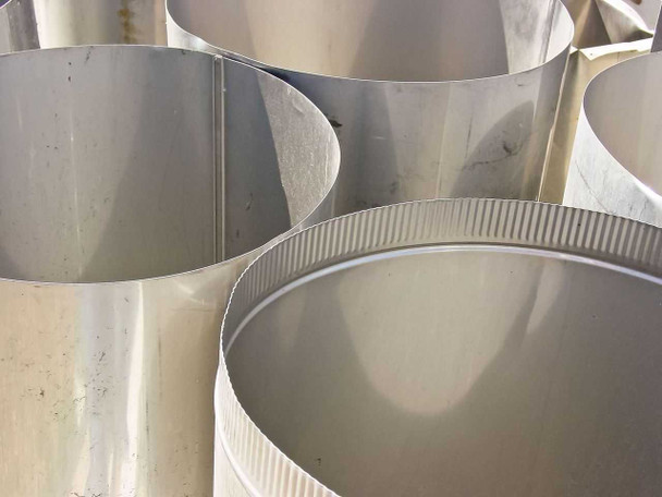 Close-up of large stainless steel round cylindrical duct sections showing corrugated locking seam at base