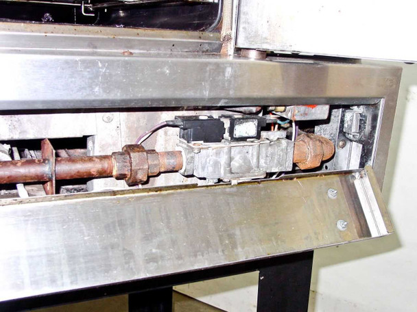Rear lower access panel open showing heavily rusted gas supply pipe, gas valve, and control components with corrosion on fittings