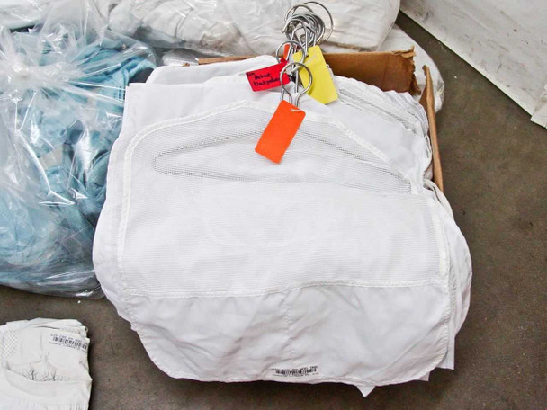 White Gore-Tex cleanroom smock or top on hanger with orange and yellow tags attached, additional blue garment bags in background