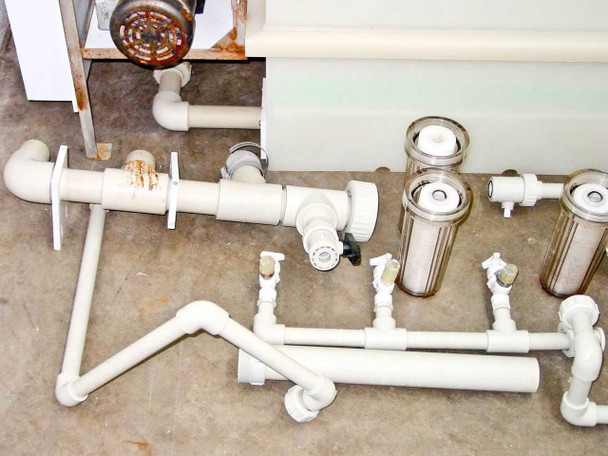 PVC pipe manifold assembly with inline filter housings and ball valves showing signs of rust on center pipe section — side view