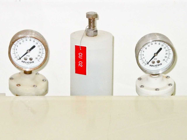 Two Helicoid PSI pressure gauges flanking a white polypropylene component on top of HDPE tank — close-up with red asset tag CU 02