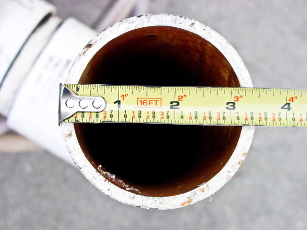 Tape measure across shell nozzle opening from above showing approximately 4 in inner diameter — rust and corrosion on interior surface